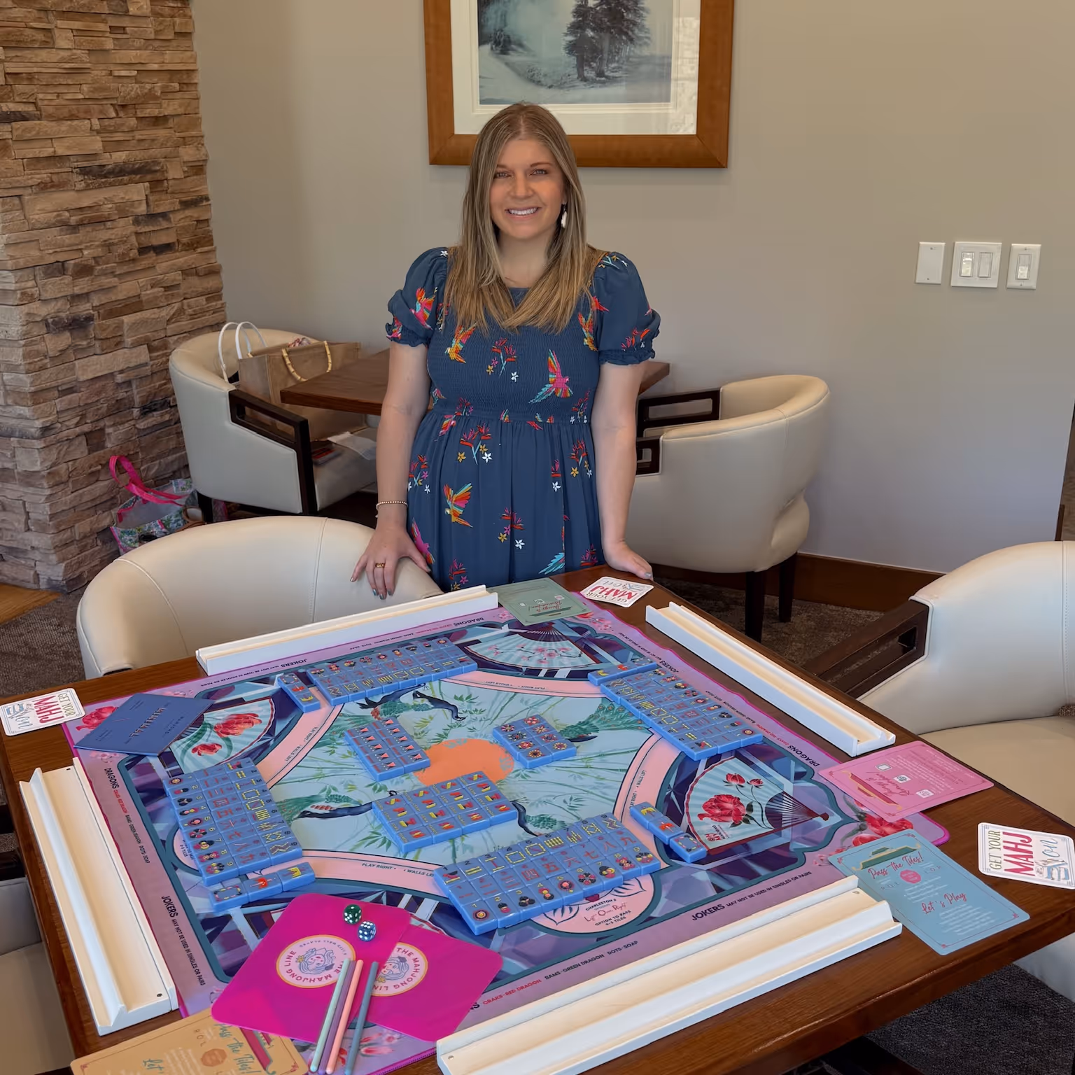 Courtney behind a fully set Mahjong Standard table — mat, racks, tiles and the card laid out — in a Castle Pines living room