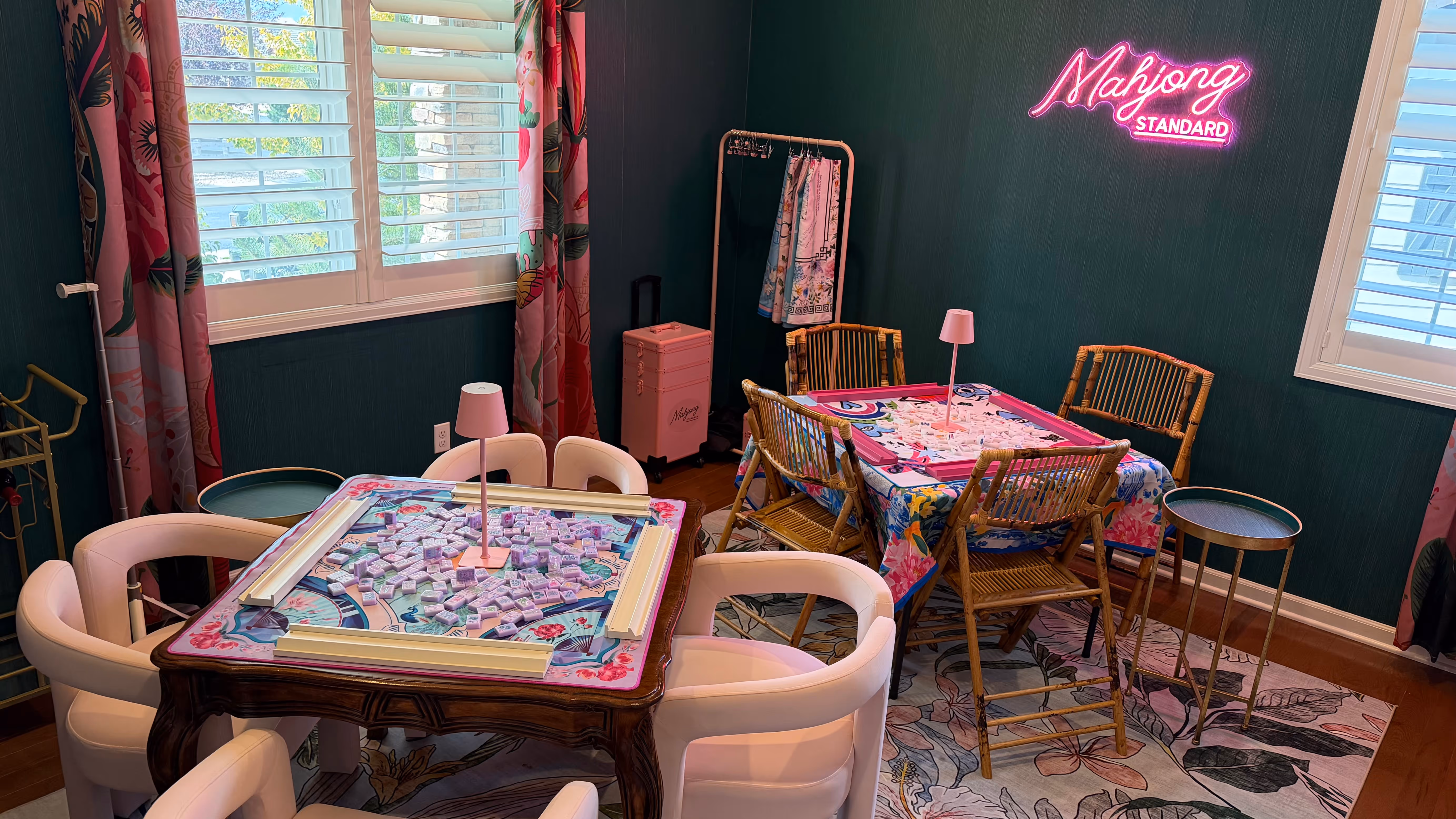 Courtney's home mahjong room in Backcountry, Highlands Ranch: two tables set for play under a glowing pink Mahjong Standard neon sign on a dark teal wall