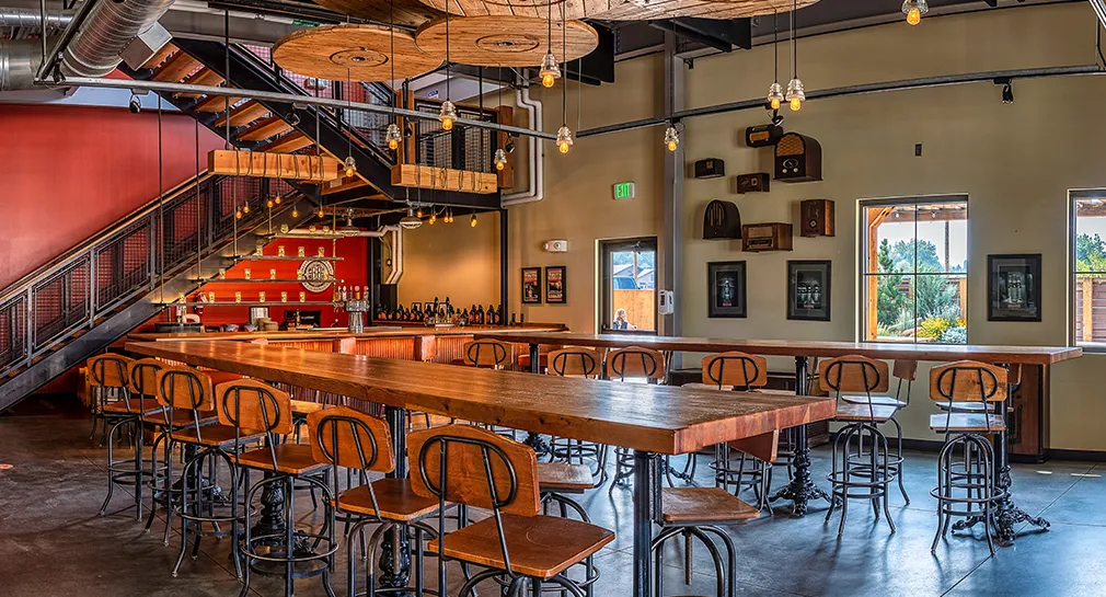 The Breckenridge Brewery tasting room in Littleton, long reclaimed-wood tables under warm pendant lights with the bar and staircase behind