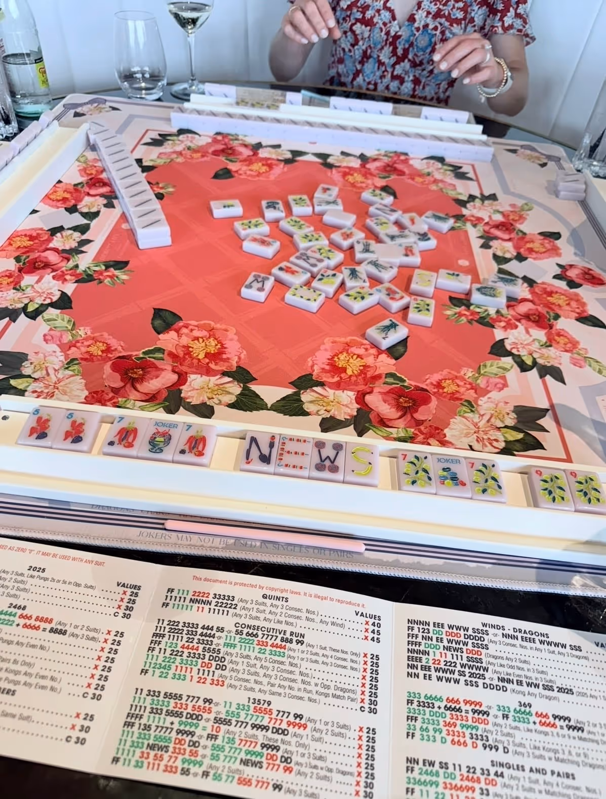 American mahjong tiles tumbling across a gorgeous floral-print mat at the start of a game, hands ready to begin the wash