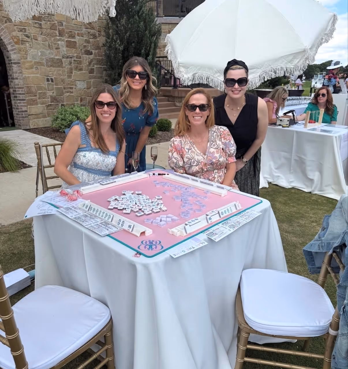An outdoor garden table dressed for mahjong, friends gathered around it