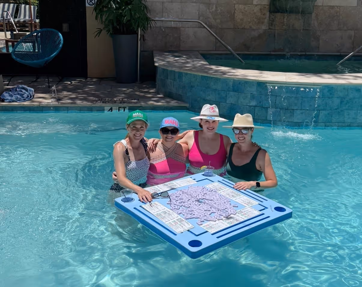 Friends playing mahjong on a floating table in the pool on a summer afternoon